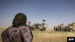 A Syrian woman looks at U.S. and Russian soldiers in the northeastern Syrian town of Malikiyah at the border with Turkey, June 3, 2020. 