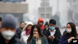 A woman uses a scarf and others wear masks to cover their face from pollutants as they walk along a street on a polluted day in Beijing, Tuesday, Dec. 8, 2015.